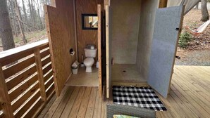 Una terraza de madera con una pequeña construcción de madera que contiene un inodoro y una zona de ducha.