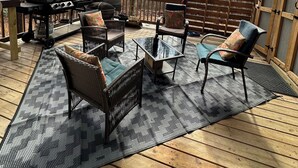 Una terraza techada al aire libre con mobiliario de mimbre, una parrilla y vistas a un bosque.