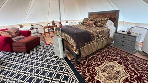 Habitación tipo alojamiento en tienda de campaña, con cama, sofá rojo, mesita de noche y alfombra estampada.