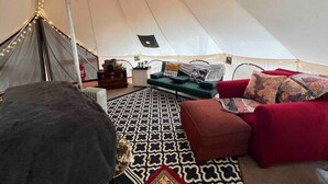 Interior de una carpa con un tapete estampado, sofás rojos y verdes, y una mesita con objetos.