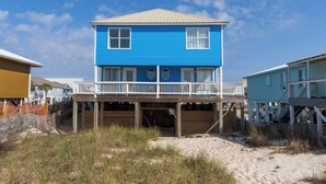Ein zweistöckiges Strandhaus mit einer Holzterrasse und einer überdachten Veranda.