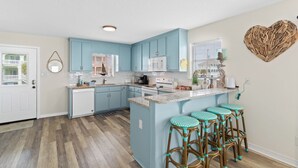 A kitchen with blue cabinets, a white microwave, and a central island with bar stools. - AOK Oasis House by Liquid Life (Fort Morgan)