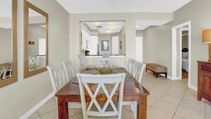 Un comedor con mesa de madera y sillas blancas, un espejo grande en la pared y un ventilador de techo.