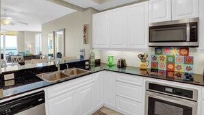 Una cocina moderna con armarios blancos, encimera negra, electrodomésticos de acero inoxidable y salpicadero de colores.