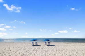 Uma praia com dois guarda-sóis azuis e cadeiras de praia.