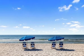 A beach with two blue umbrellas and beach chairs.