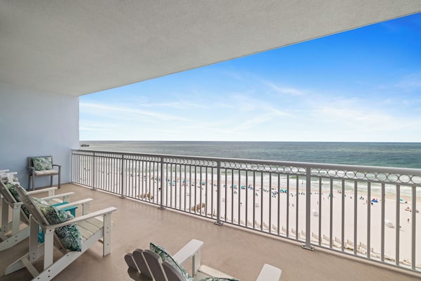 Un balcon donnant sur la plage, avec des chaises blanches et une balustrade.