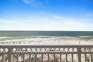A beach with a railing in the foreground, sandy beach, and ocean.
