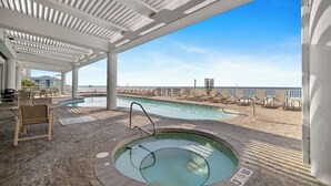 Un espace piscine abrité, doté de chaises longues et d’un jacuzzi, avec vue sur la plage.