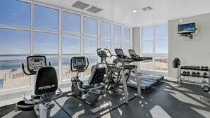 A gym with cardio machines, dumbbells, and a TV on the wall.
