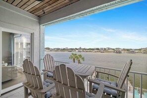 A balcony with a view of a body of water, wooden chairs, and a table.