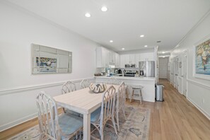 A modern kitchen with white cabinetry, a central island, and a dining area with a wooden table and wicker chairs.