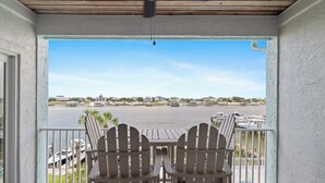Une terrasse couverte avec deux fauteuils Adirondack, une table et une vue sur une marina avec des bateaux et des maisons de l’autre côté d’une étendue d’eau.