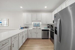 A modern kitchen with white cabinetry, a stainless steel refrigerator, and a dishwasher.