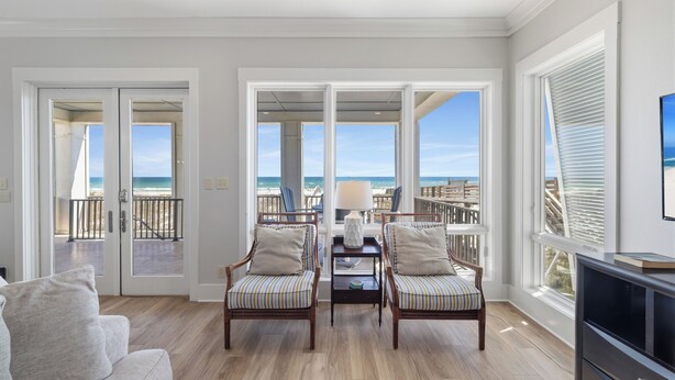 A spacious living room with a view of the beach, two armchairs, a sofa, and a TV. - Finntastic Beachfront House by Liquid Life (Gulf Shores)