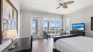A hotel room with a bed, a desk, a chair, a TV, a ceiling fan, and a balcony with a view of the ocean. - Finntastic Beachfront House by Liquid Life (Gulf Shores)