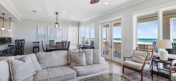 Ein geräumiger Wohnbereich mit großem Sofa, Esstisch und Stühlen, einer Küchenzeile und einem Balkon mit Blick auf den Strand.