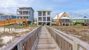 A wooden boardwalk leading to a beachfront property with multiple buildings, including a two-story house with a balcony and a larger building with a balcony. - Finntastic Beachfront House by Liquid Life (Gulf Shores)