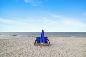 Een strand met twee blauwe strandstoelen en een blauwe parasol.