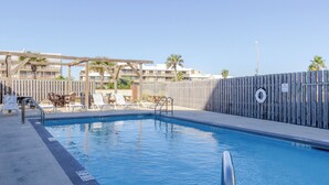 Une piscine avec une terrasse en bois, des chaises longues et une clôture en bois.