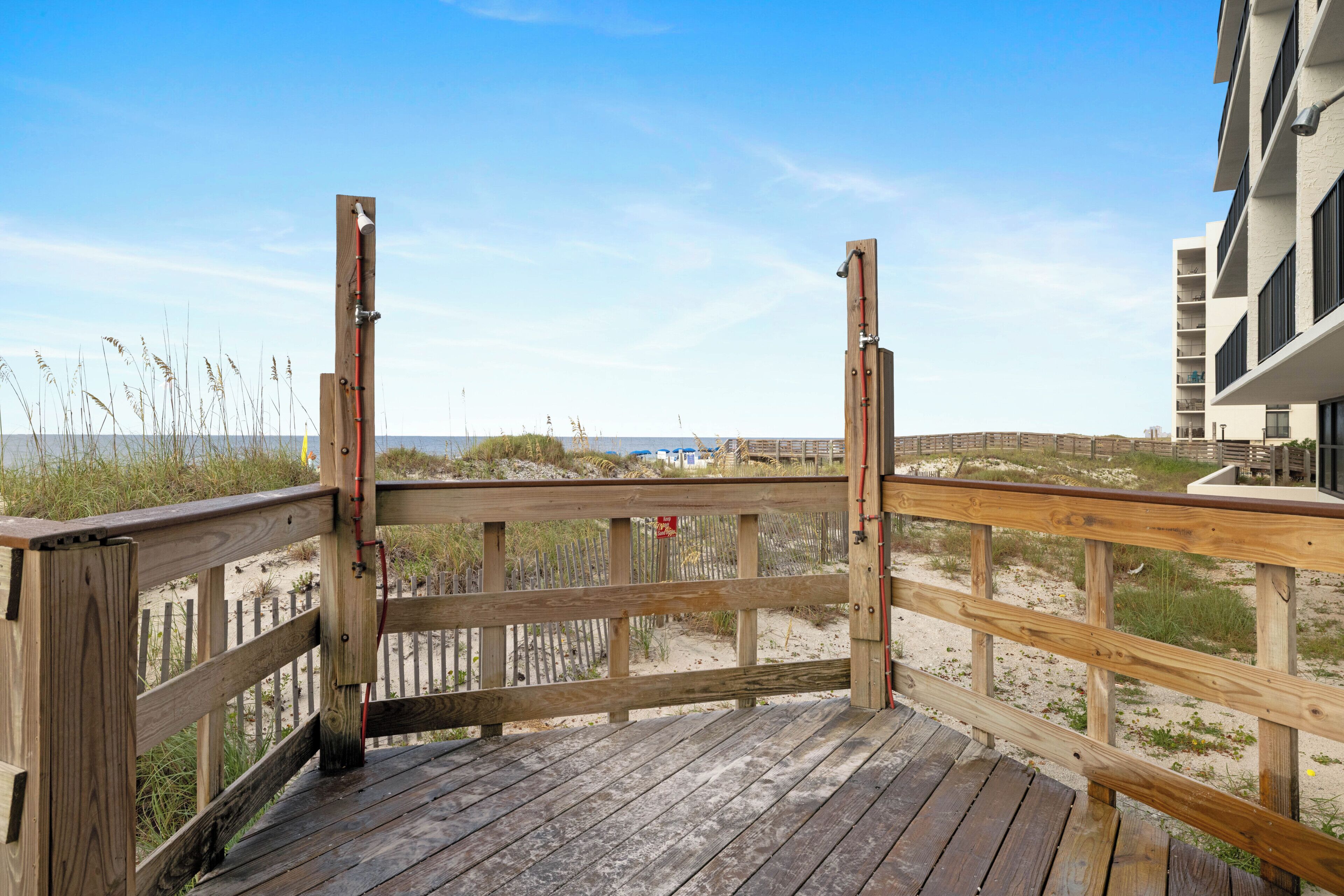 En træterrasse med udsigt til stranden og en bygning i baggrunden.