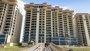 A multi-story residential building with balconies, a central staircase, and a surrounding fence.