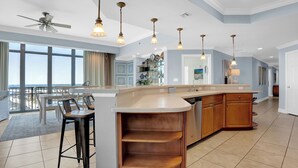 A spacious kitchen with a large island, bar stools, and pendant lighting. - Phoenix West 1601 by Liquid Life (Orange Beach)