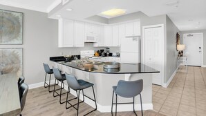 A modern kitchen with white cabinets, a central island with bar stools, and a dining area with a wooden table and chairs. - San Carlos 1108 by Liquid Life (Gulf Shores)