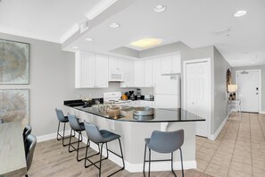 A modern kitchen with white cabinets, a central island with bar stools, and a dining area with a wooden table and chairs.