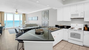 A modern kitchen with white cabinets, a black countertop, and a built-in oven. There is a dining area with a table and chairs, and a large window offering a view of the ocean. - San Carlos 1108 by Liquid Life (Gulf Shores)