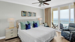 A hotel room with a large bed, a ceiling fan, a balcony with a view of the ocean, and a chair. - San Carlos 1108 by Liquid Life (Gulf Shores)