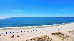 A beach with rows of umbrellas and beach chairs, a flag, and dunes. - San Carlos 1108 by Liquid Life (Gulf Shores)