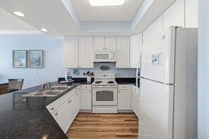 A modern kitchen with white cabinets, a black countertop, a built-in oven, and a refrigerator. - San Carlos 505 by Liquid Life (Gulf Shores)