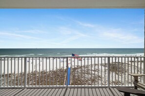 A beach view from a balcony with a railing, a flag, and a bench.