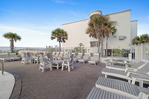 Une terrasse sur le toit, avec des chaises longues et des tables blanches, des palmiers et un bâtiment blanc en arrière-plan.