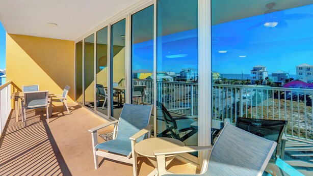 Un balcon avec plusieurs chaises et une table, de grandes fenêtres en verre et une vue sur des bâtiments au loin.