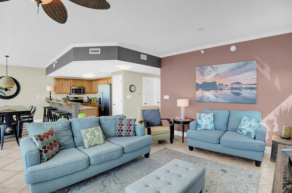 A living room with a blue sofa, a matching ottoman, and a dining area with a table and chairs.