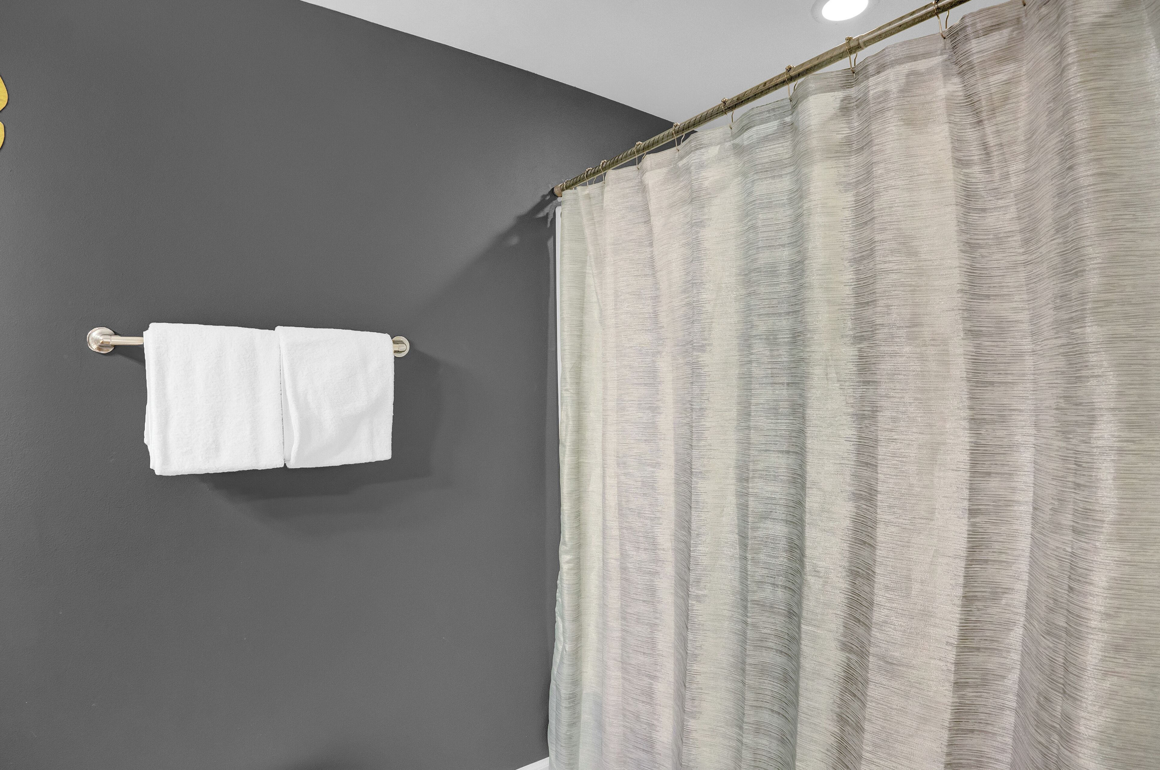A bathroom with a dark gray wall, a white towel hanging on a metal towel rack, and a striped shower curtain.