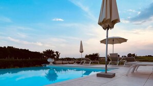 A swimming pool with lounge chairs and umbrellas, surrounded by a landscaped area with trees and a clear sky.
