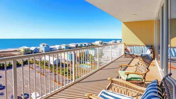Un balcon avec des meubles en osier, une vue sur la plage et un espace de stationnement.