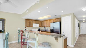 Una cocina con armarios de madera, microondas, refrigerador y una zona de bar con sillas.