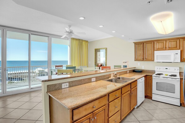 Una cocina moderna con una isla grande, microondas, horno y vistas al océano a través de amplios ventanales.