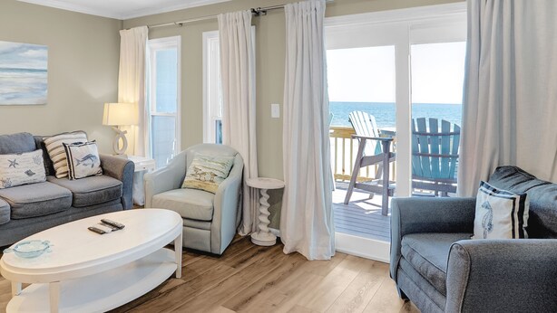 Ein Wohnzimmer mit Sofa, Sessel und Couchtisch, einem Deckenventilator und Meerblick durch große Fenster.