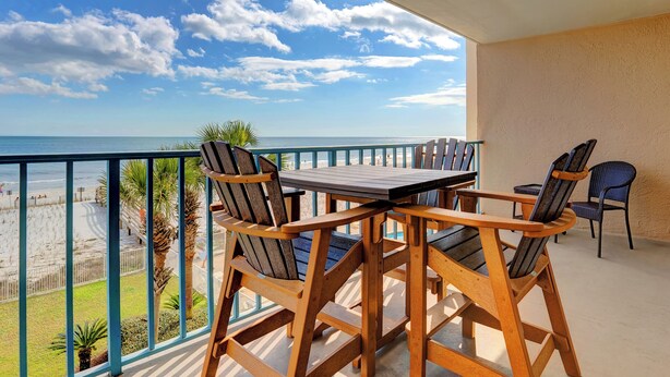 A balcony with a wooden table and chairs, overlooking a beach with a clear sky. - Surfside Shores 1302 by Liquid Life (Gulf Shores)