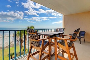 Een balkon met een houten tafel en stoelen, met uitzicht op een strand en een heldere lucht.