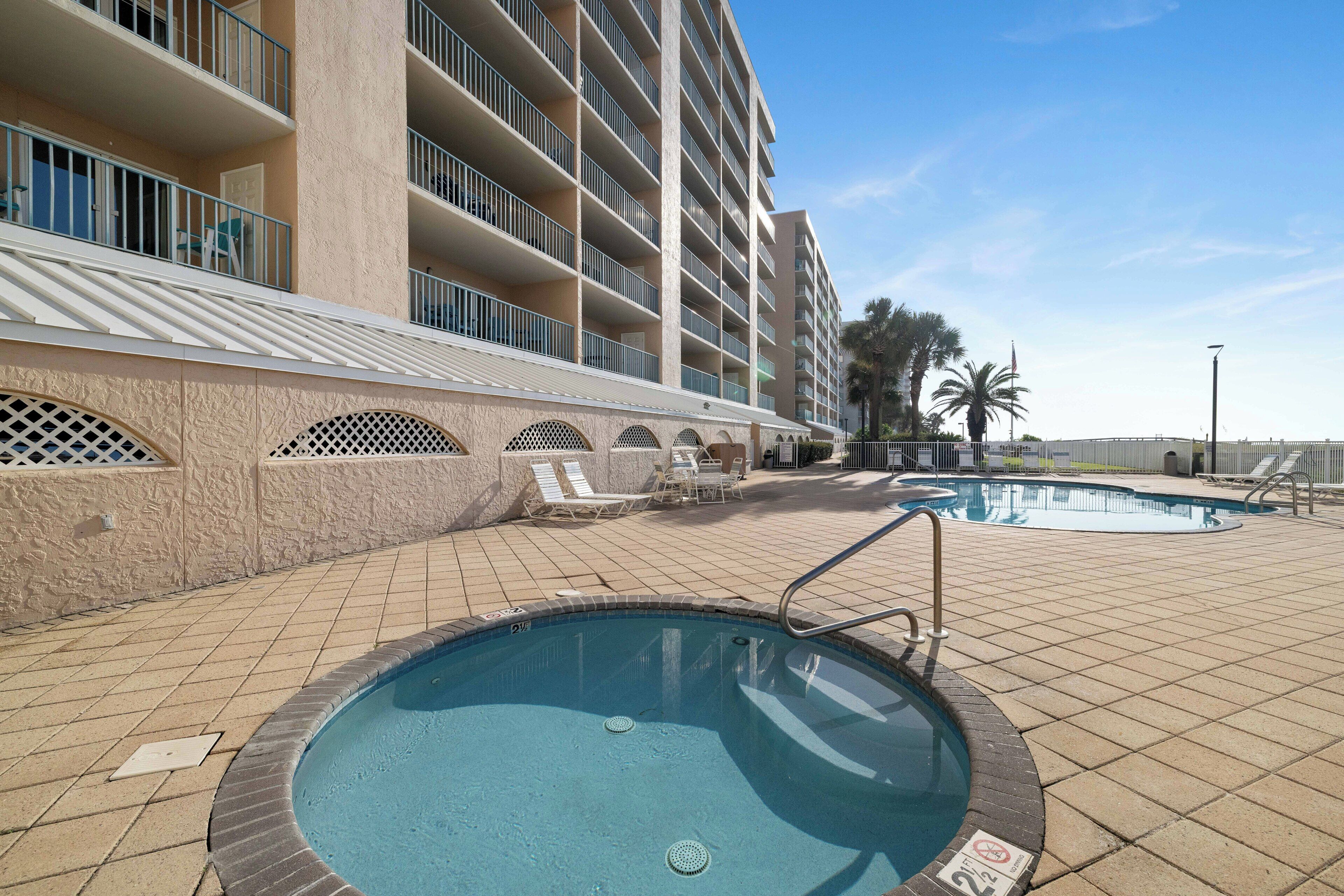 A hotel pool area with a large pool, lounge chairs, and a building with multiple balconies.
