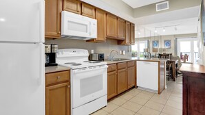 A modern kitchen with wooden cabinets, white appliances, and a central island. - Surfside Shores 1302 by Liquid Life (Gulf Shores)