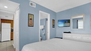 A bedroom with a bed, a television, a bathroom, and a kitchen area. - Surfside Shores 1302 by Liquid Life (Gulf Shores)