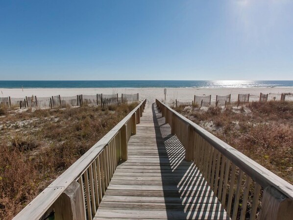A wooden boardwalk leading to a beach with a clear sky.