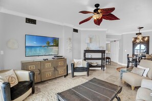 A living room with a TV, sofa, coffee table, and ceiling fan.